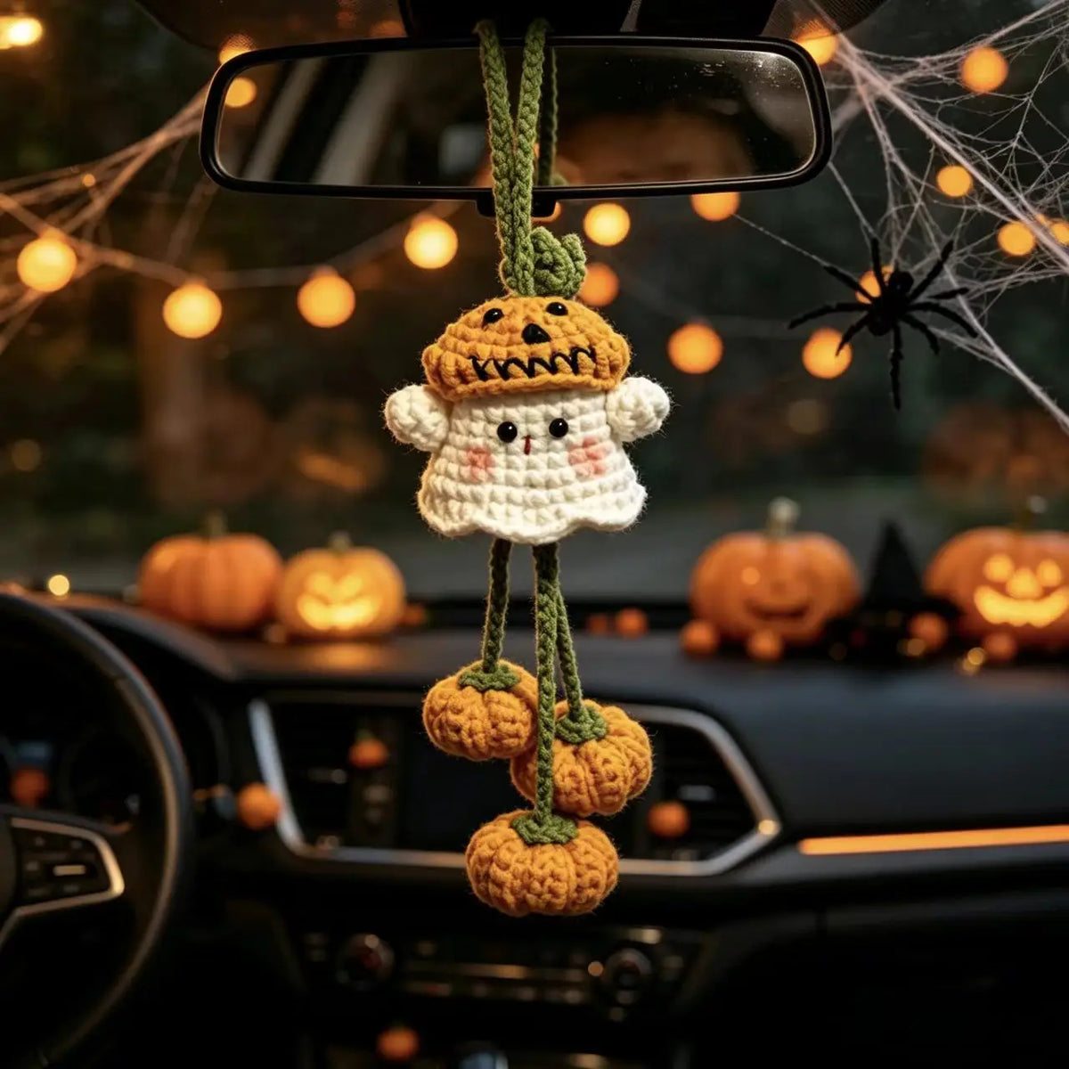 Crochet pumpkin ghost charm hanging from a car rear-view mirror with Halloween decor