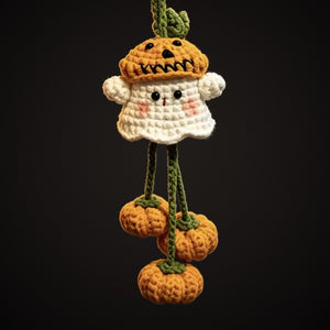 Crochet ghost with pumpkin hat and three dangling mini pumpkins on a dark background